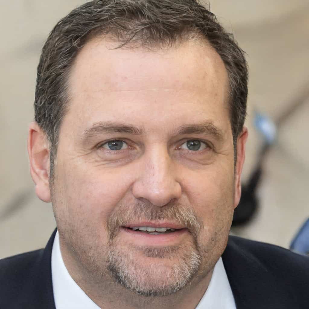 Portrait of a smiling man with short hair and a suit, looking at the camera with a neutral background.
