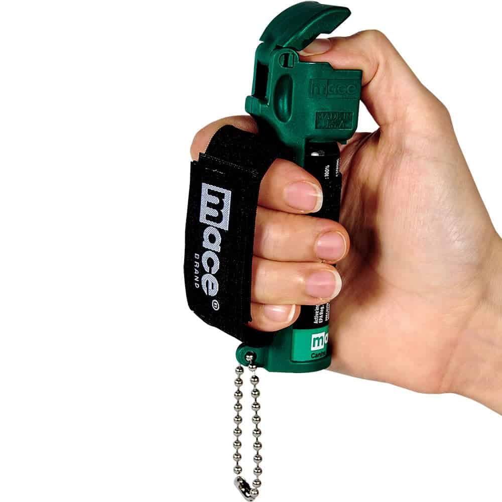 Hand holding green pepper spray canister with black strap and safety chain for self-defense.