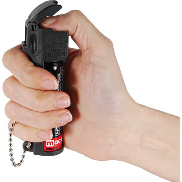 Hand holding a pepper spray canister with a protective flip-top, ready for personal safety use.