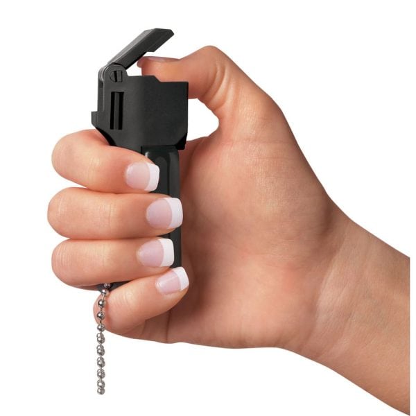 Hand holding a black pepper spray with a thumb on the safety lock, ready for use.