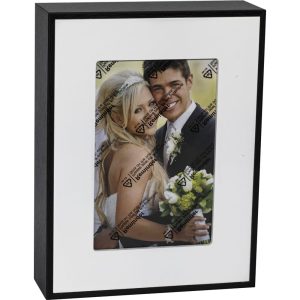 Framed photo of a smiling couple at their wedding, with protective film on the glass and a black frame.