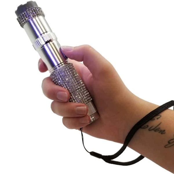 Hand holding a silver rhinestone flashlight with strap, isolated on white background.