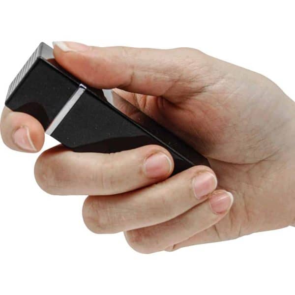 Hand holding a black rectangular device with thumb resting on button, isolated on white background.