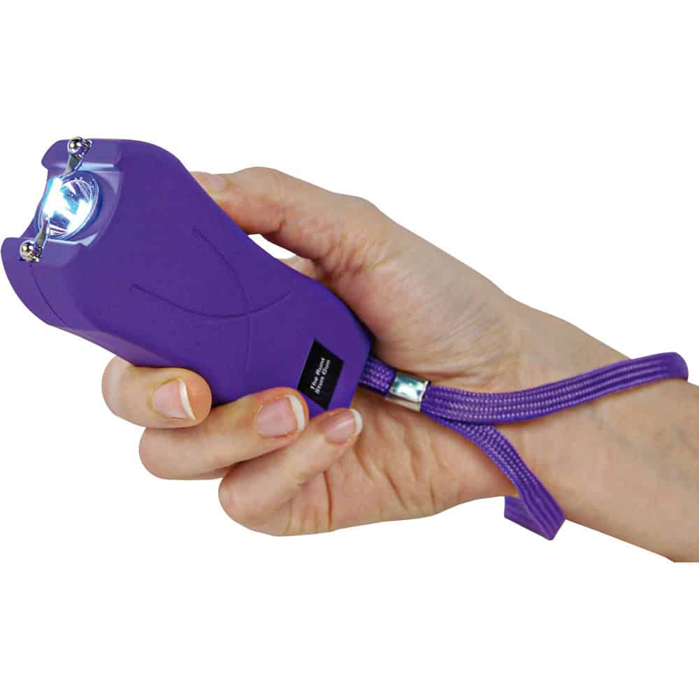 Hand holding a purple stun gun with a safety strap for personal protection.