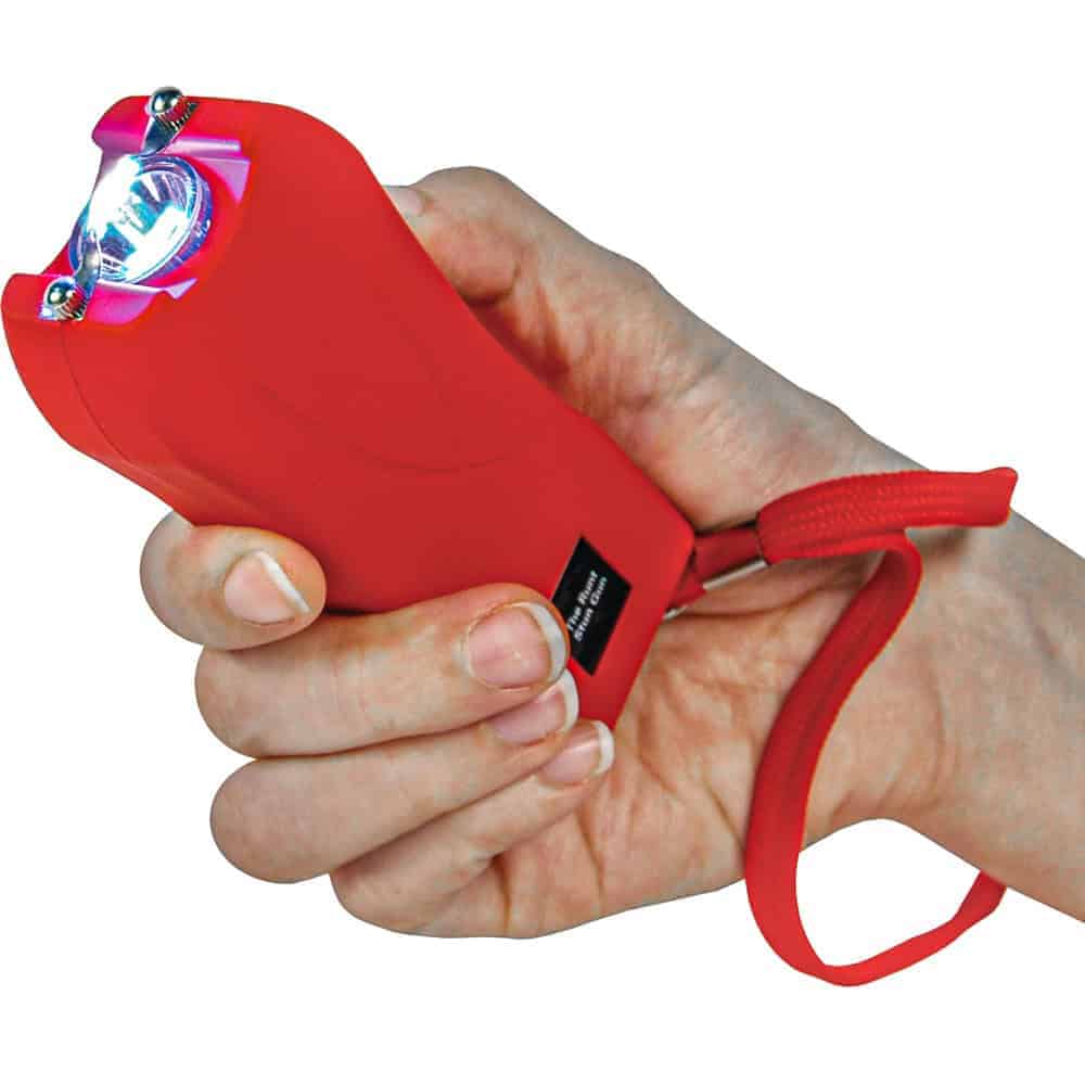 Red handheld stun gun with a wrist strap, showing bright arc at the top, held in a person's hand.