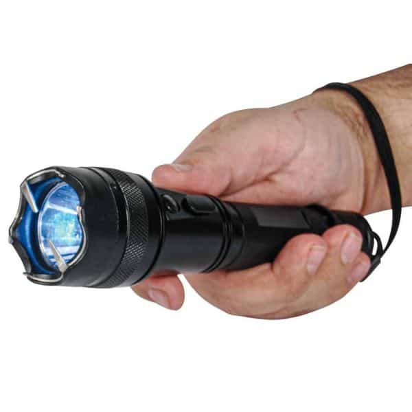 Hand holding a black stun gun flashlight with glowing blue light, close-up.