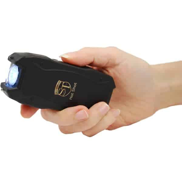 Hand holding a black stun gun with blue light, close-up for self-defense demonstration.