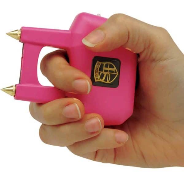 Pink handheld personal safety device with dual spikes, held in a hand, ready for use.