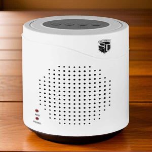 White tabletop sound machine with control buttons on top, placed on a wooden surface.