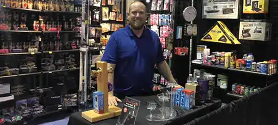 Man at a trade show booth showcasing various products on display shelves.