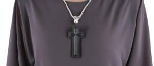 Black cross pendant on silver chain necklace over dark fabric background.