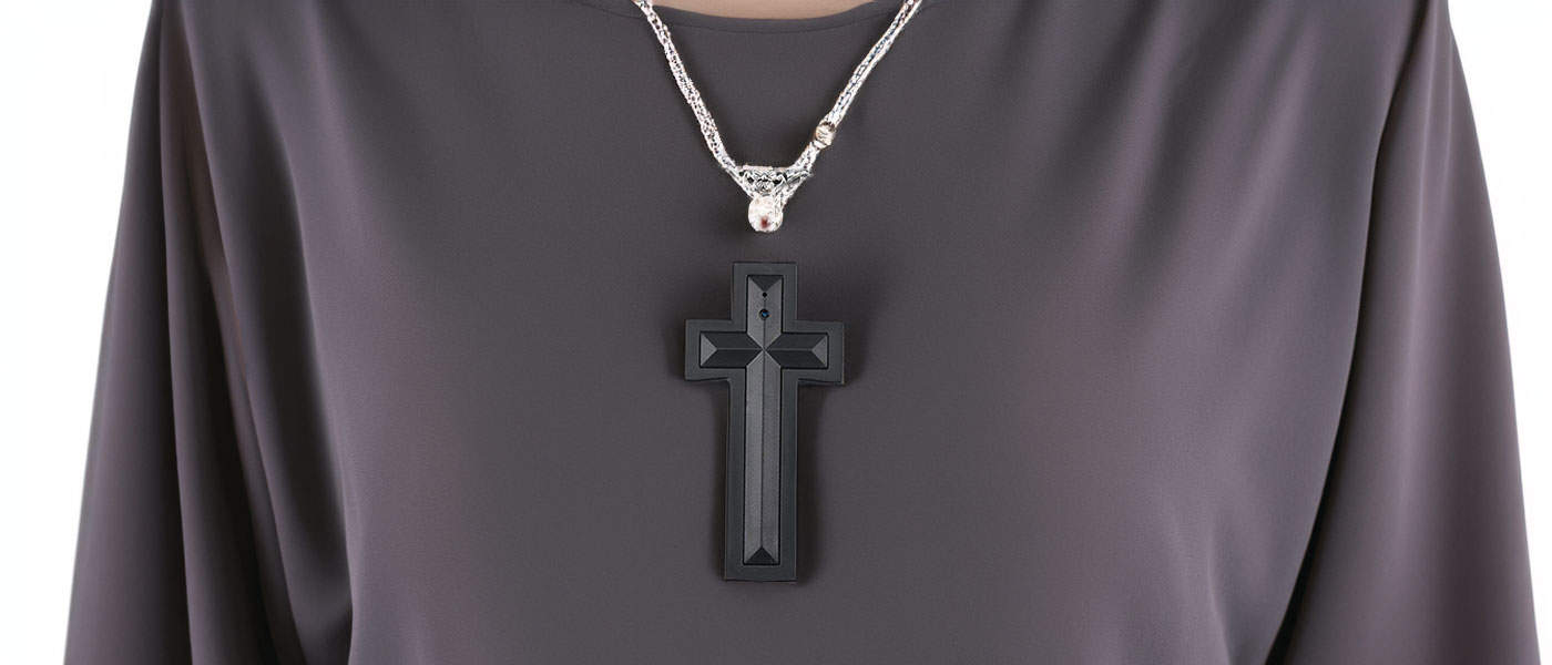 Black cross pendant on silver chain necklace over dark fabric background.