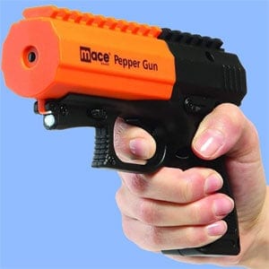 Hand holding an orange Mace pepper spray gun for self-defense against a blue background.