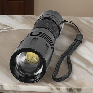 Black tactical flashlight with wrist strap on marble surface.