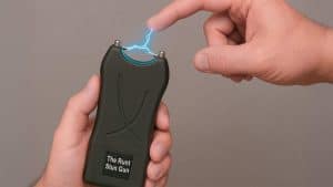 Hand holding The Runt Stun Gun, generating electric spark to finger. Personal safety device demonstration.